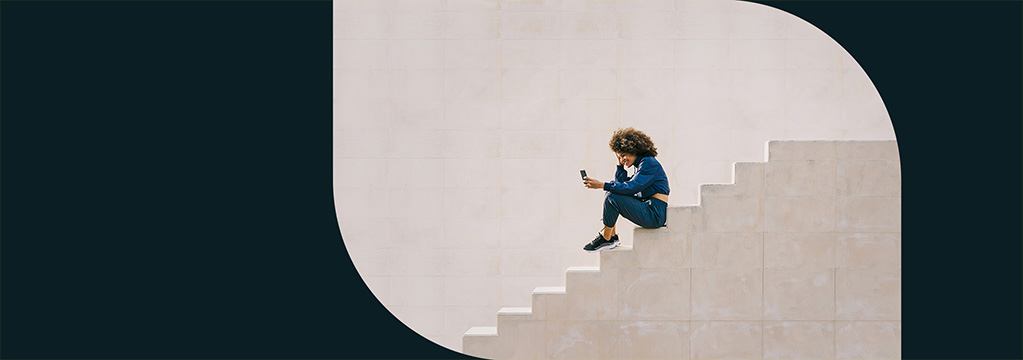 Eine sportliche Frau sitzt auf einer Treppe und schaut auf ihr Smartphone.