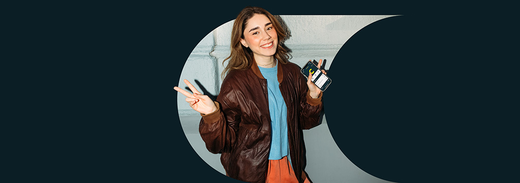 Ein Mädchen in Shirt und Bomberjacke lächelt und macht dabei das Peace-Zeichen.