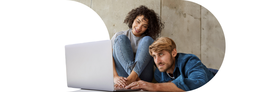 Eine junge, lockige Frau und ein blonder Mann sitzen gemeinsam auf dem Boden vor einem Laptop. Sie nutzen den Portfolio-Planer als Starthilfe für die Geldanlage.