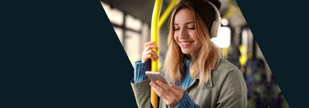 Eine junge Frau mit Kopfh&ouml;rern schaut unterwegs im Bus auf ihr Smartphone.