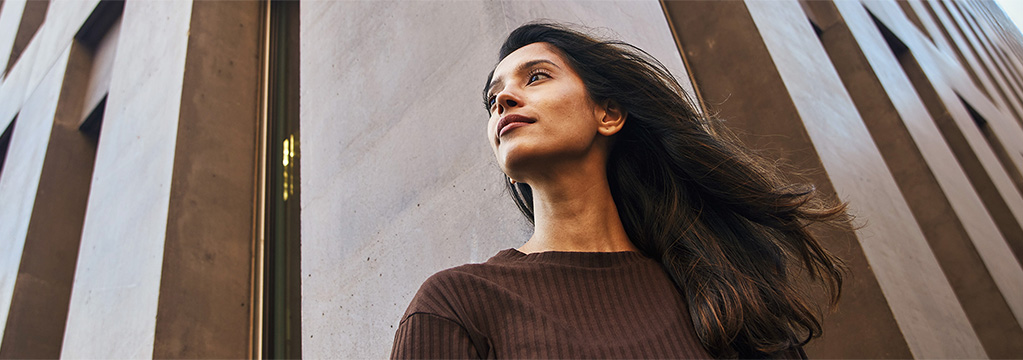 Frau steht vor hoher Fassade und blickt ruhig nach oben