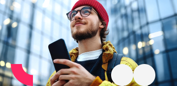 Ein junger Mann schaut gl&uuml;cklich von seinem Smartphone auf in Richtung Himmel.