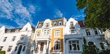 Eine Straßenzeile mit prächtigen Stadtvillen leuchtet hell vor einem blauen Himmel.